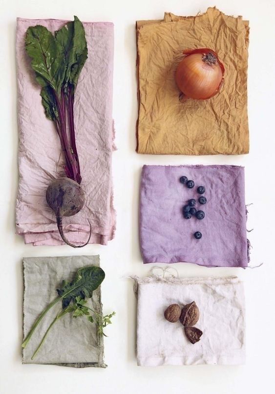 an onion, beet, blueberries, greens, and nuts lying against dyed fabrics.