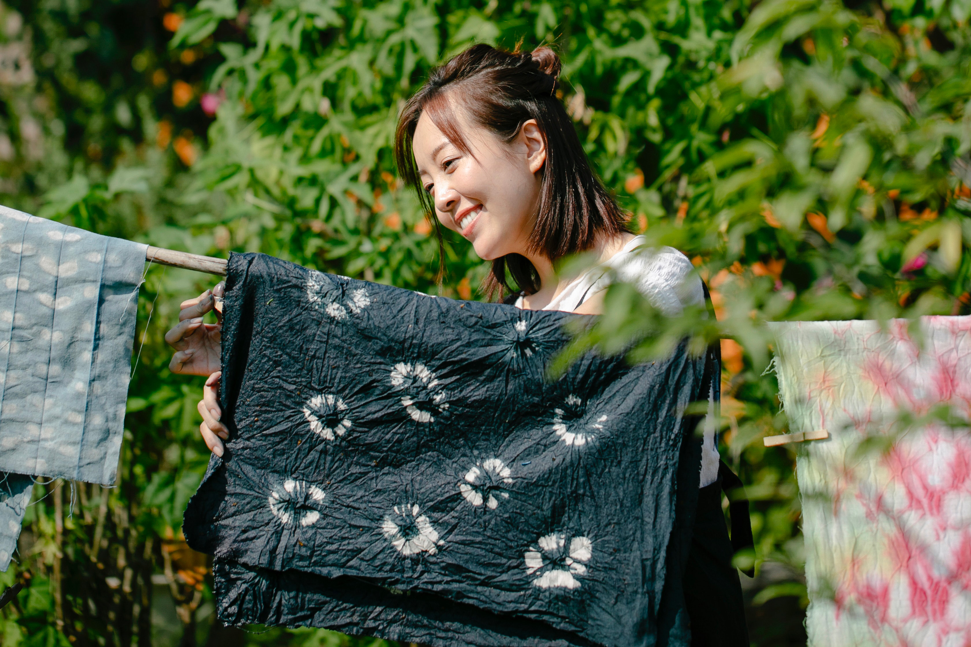 Joyful woman near rope with painted fabrics.